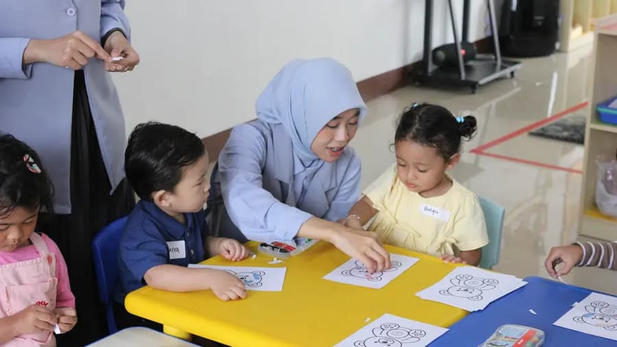 Guru membimbing murid mewarnai di meja kelas
